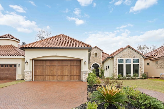 mediterranean / spanish house with a garage, stone siding, decorative driveway, and stucco siding