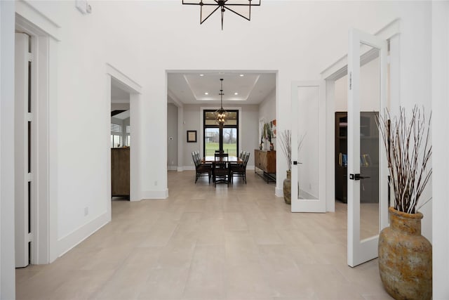 foyer with a tray ceiling, french doors, recessed lighting, an inviting chandelier, and baseboards