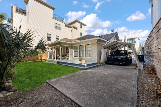 back of property with brick siding, a yard, fence, a carport, and driveway