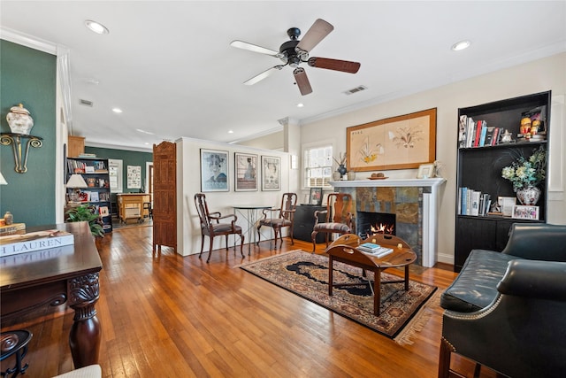 living room with ornamental molding, wood-type flooring, visible vents, and a tiled fireplace