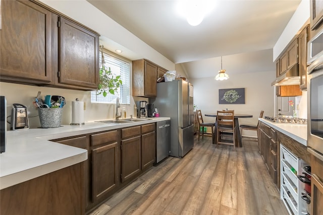 kitchen featuring appliances with stainless steel finishes, light countertops, a sink, and wood finished floors