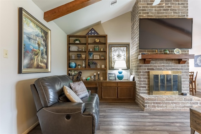 living area with vaulted ceiling with beams, a brick fireplace, wood finished floors, and visible vents