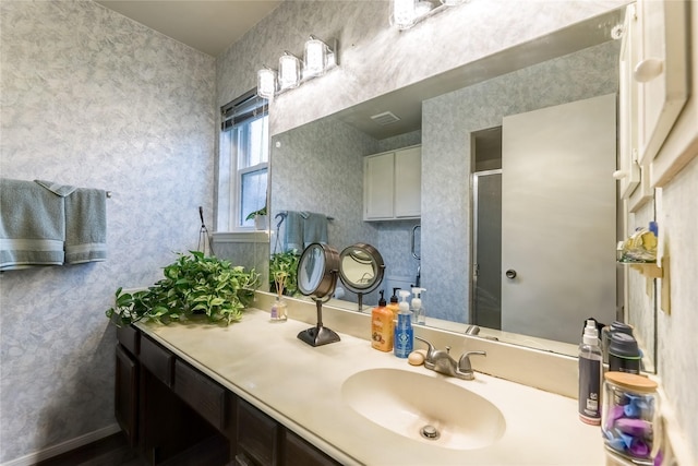 full bath with wallpapered walls, vanity, and a stall shower