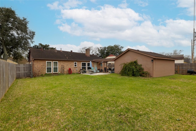 rear view of property featuring a patio, a fenced backyard, brick siding, a yard, and a chimney