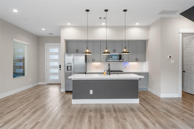 kitchen with gray cabinets, light countertops, light wood-style flooring, decorative backsplash, and appliances with stainless steel finishes