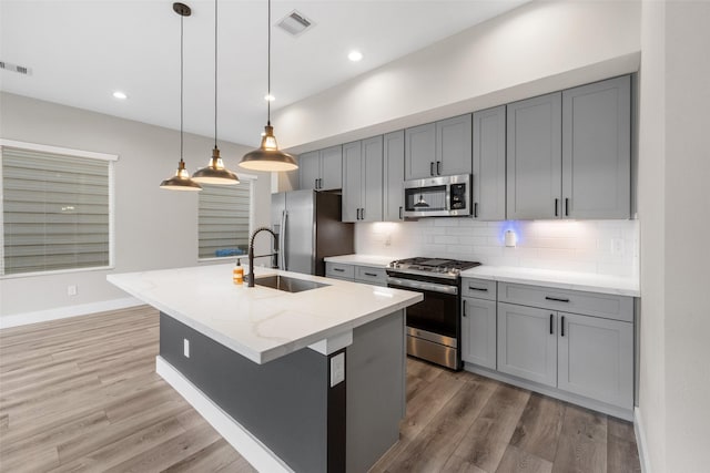 kitchen with appliances with stainless steel finishes, light wood-style floors, a sink, and tasteful backsplash