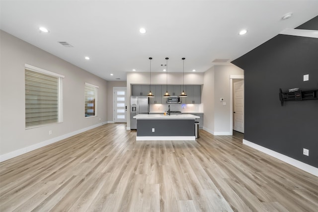 kitchen with stainless steel appliances, light wood finished floors, light countertops, and a kitchen island with sink