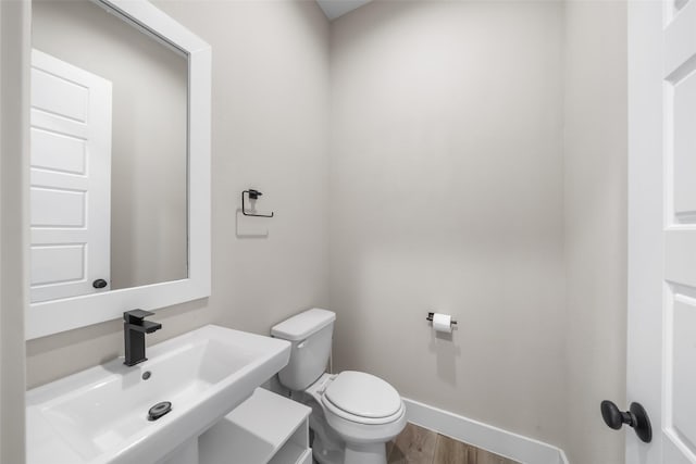 bathroom featuring toilet, baseboards, a sink, and wood finished floors