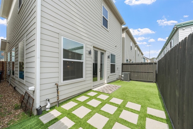 rear view of property with french doors, a lawn, a fenced backyard, and central air condition unit