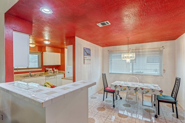 kitchen featuring tile counters, white cabinets, visible vents, and a sink