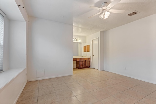 spare room with light tile patterned floors, visible vents, baseboards, ceiling fan, and a textured ceiling