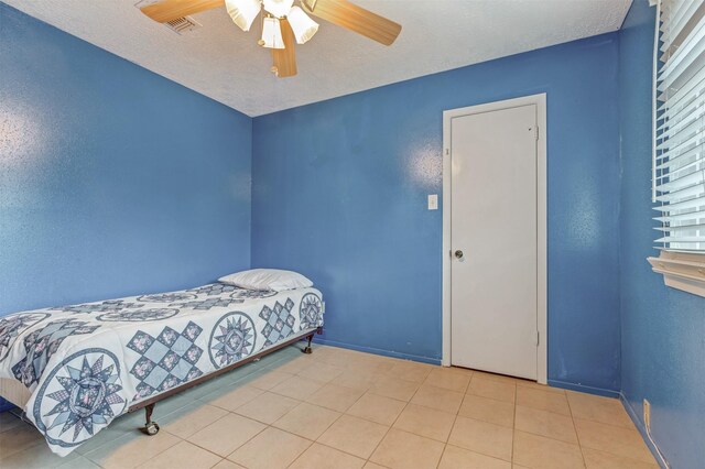 bedroom with ceiling fan, a textured ceiling, visible vents, baseboards, and tile patterned floors