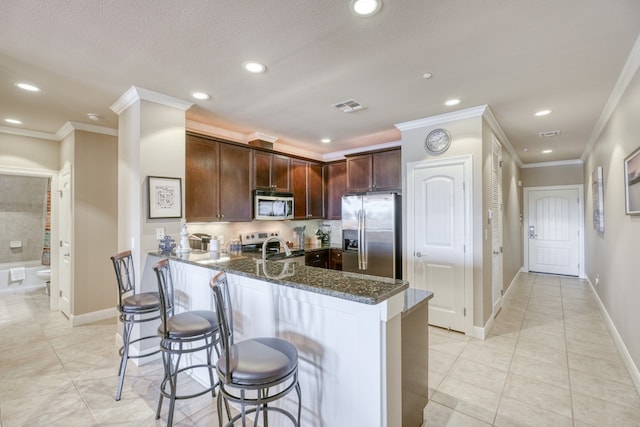 kitchen with visible vents, a breakfast bar, dark stone countertops, a peninsula, and stainless steel appliances