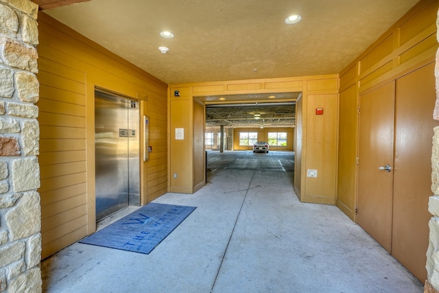 hall with wood walls, recessed lighting, and elevator