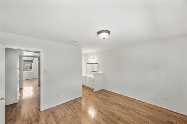 empty room featuring light wood finished floors, visible vents, and baseboards