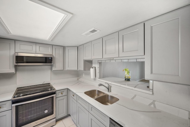 kitchen with light stone counters, gray cabinets, visible vents, appliances with stainless steel finishes, and a sink