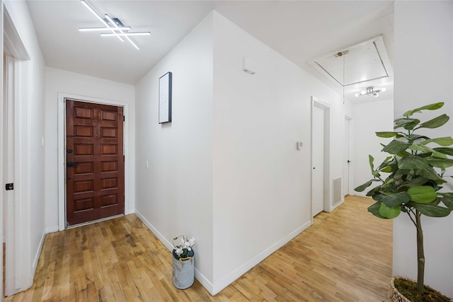 corridor with attic access, visible vents, baseboards, and light wood-style flooring