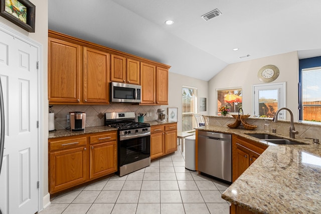 kitchen with light tile patterned flooring, appliances with stainless steel finishes, brown cabinetry, and a sink