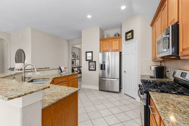 kitchen featuring light tile patterned floors, arched walkways, a sink, decorative backsplash, and stainless steel appliances