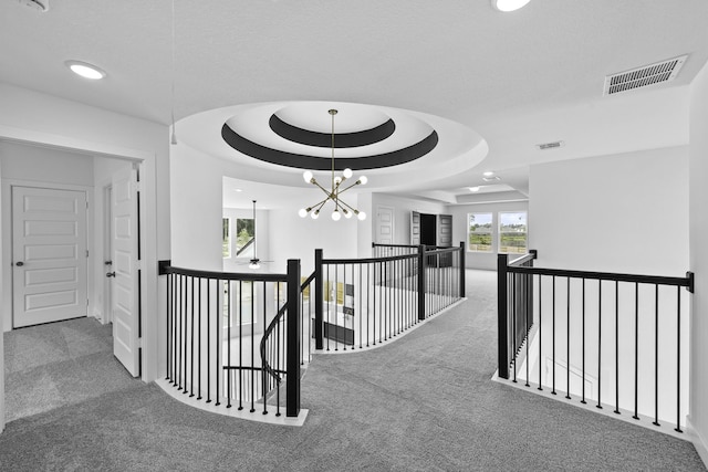 hall with carpet, visible vents, a raised ceiling, and an upstairs landing