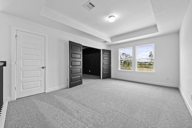 unfurnished bedroom featuring carpet, a raised ceiling, visible vents, and baseboards