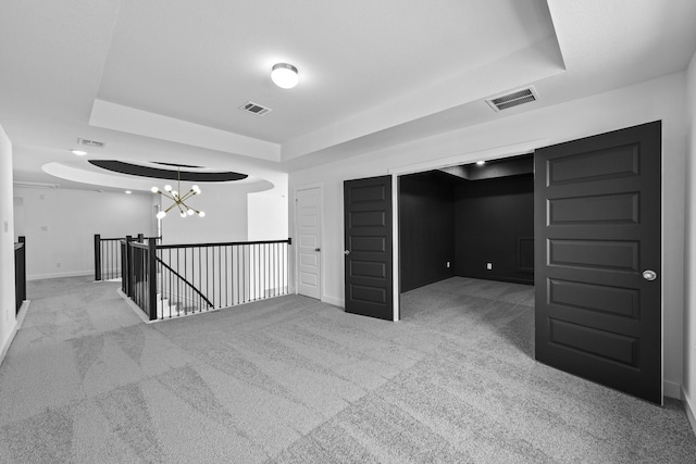 spare room with carpet flooring, a raised ceiling, visible vents, and an inviting chandelier