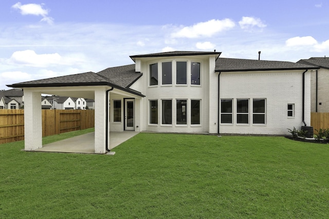 rear view of property featuring a yard, roof with shingles, fence, and a patio