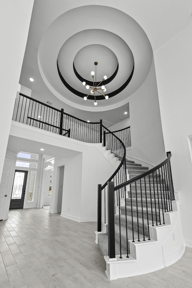 staircase featuring a tray ceiling, recessed lighting, a towering ceiling, an inviting chandelier, and baseboards