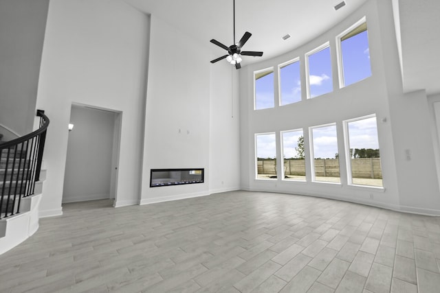 unfurnished living room featuring ceiling fan, light wood-style flooring, baseboards, stairway, and a glass covered fireplace