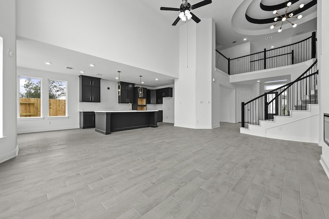 unfurnished living room with ceiling fan with notable chandelier, light wood-style flooring, recessed lighting, and stairs