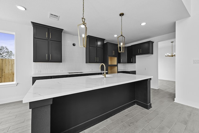 kitchen featuring visible vents, a spacious island, light wood-style flooring, light stone countertops, and a sink