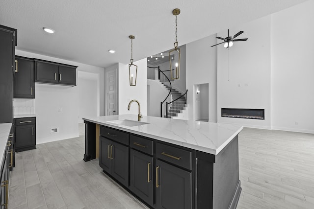 kitchen with wood finish floors, decorative light fixtures, a glass covered fireplace, a sink, and an island with sink