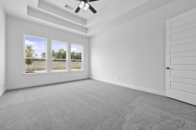 carpeted empty room featuring visible vents, a tray ceiling, ceiling fan, and baseboards