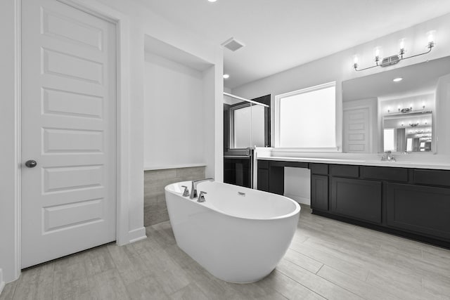 bathroom with a stall shower, visible vents, wood finished floors, vanity, and a freestanding tub