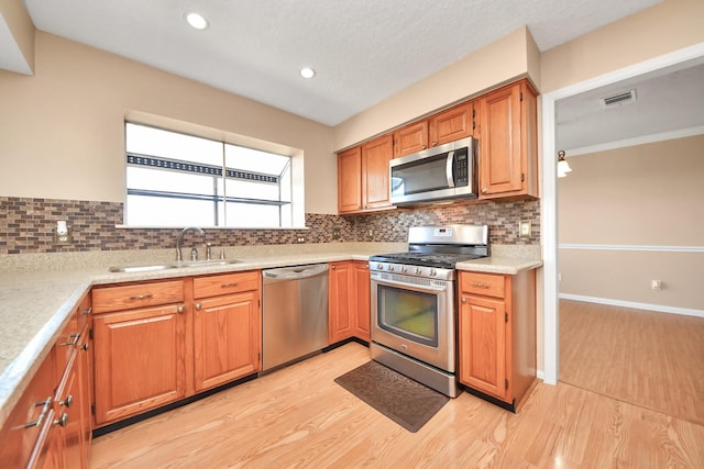 kitchen with a sink, light wood-style floors, light countertops, appliances with stainless steel finishes, and backsplash