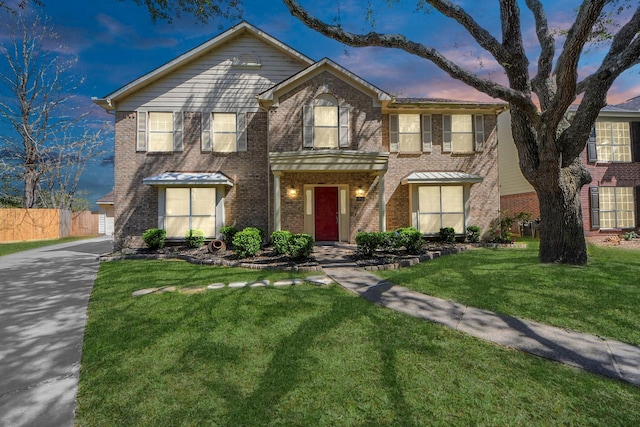 traditional home featuring a yard, driveway, brick siding, and fence