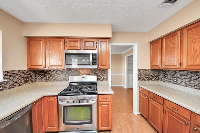 kitchen with visible vents, brown cabinets, stainless steel appliances, light wood-style floors, and backsplash