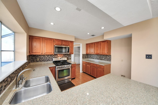 kitchen featuring tasteful backsplash, light wood-style flooring, appliances with stainless steel finishes, light countertops, and a sink