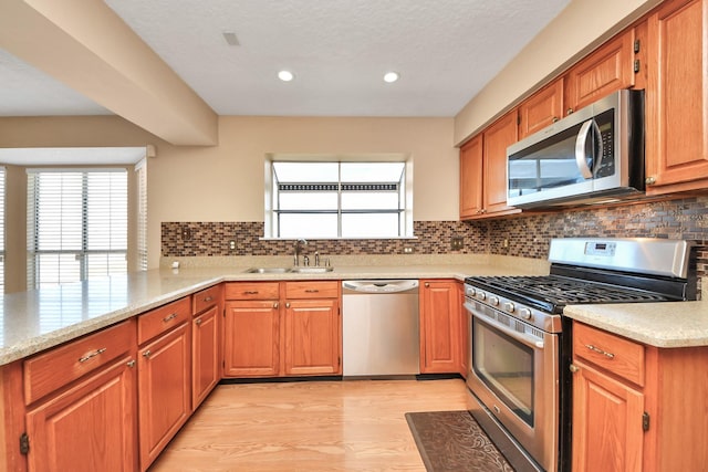 kitchen featuring light wood-type flooring, tasteful backsplash, appliances with stainless steel finishes, and a sink