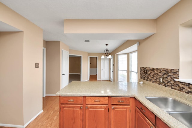 kitchen featuring a notable chandelier, visible vents, decorative backsplash, light wood-style floors, and a peninsula