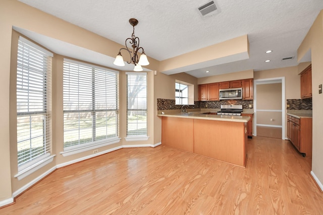 kitchen featuring stainless steel appliances, a peninsula, visible vents, backsplash, and light wood finished floors