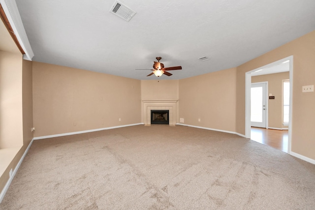 unfurnished living room with carpet, visible vents, a tiled fireplace, ceiling fan, and baseboards