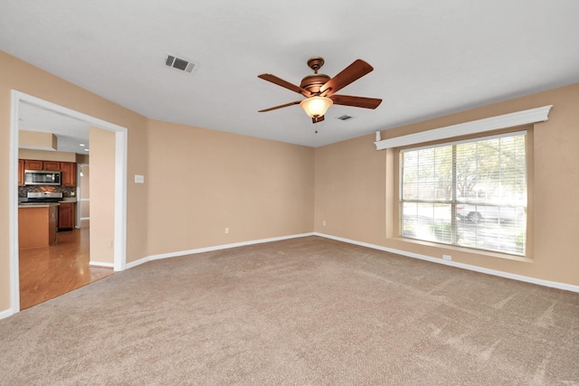 empty room with light carpet, ceiling fan, visible vents, and baseboards