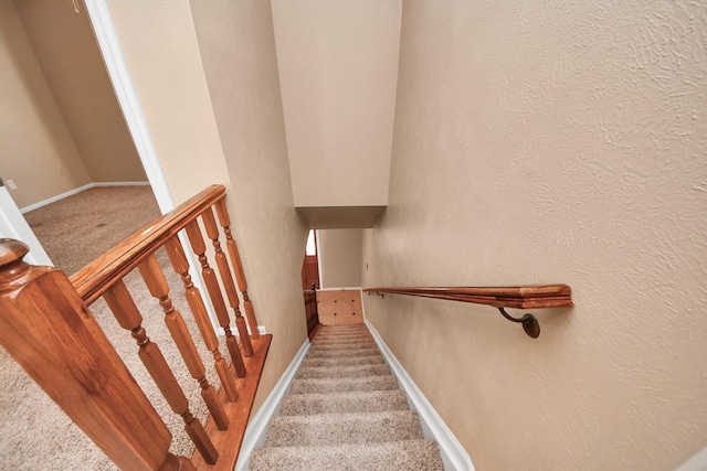 stairs with a textured wall, carpet, and baseboards