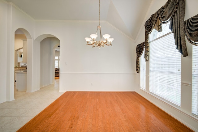 unfurnished room featuring arched walkways, light tile patterned flooring, baseboards, vaulted ceiling, and ornamental molding