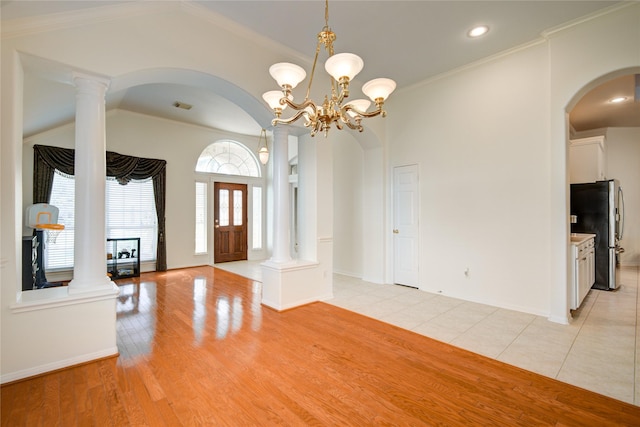 entryway featuring arched walkways, lofted ceiling, light wood-style flooring, ornamental molding, and ornate columns