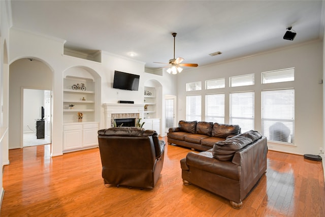 living area featuring visible vents, built in features, crown molding, light wood-type flooring, and a fireplace