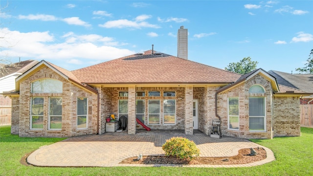 back of house with a patio, a chimney, roof with shingles, a yard, and brick siding