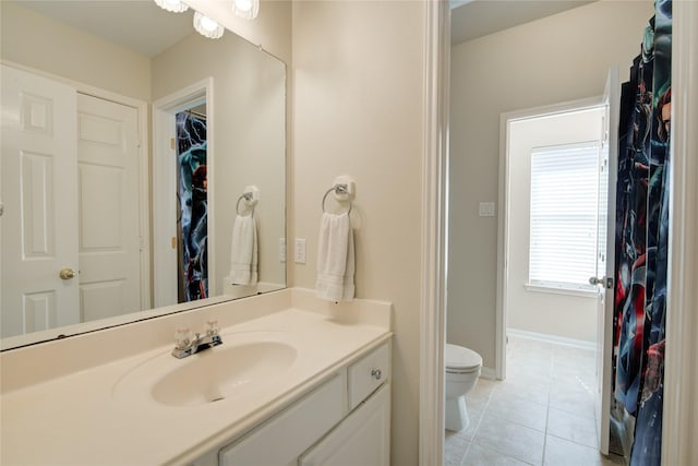 bathroom with a walk in closet, toilet, vanity, tile patterned flooring, and baseboards