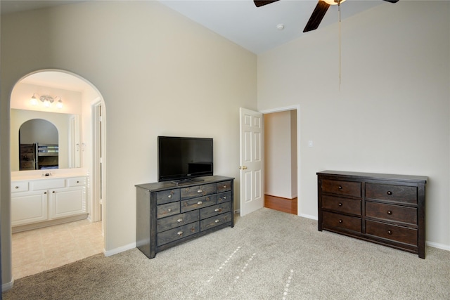 carpeted bedroom with ceiling fan, high vaulted ceiling, baseboards, and ensuite bathroom